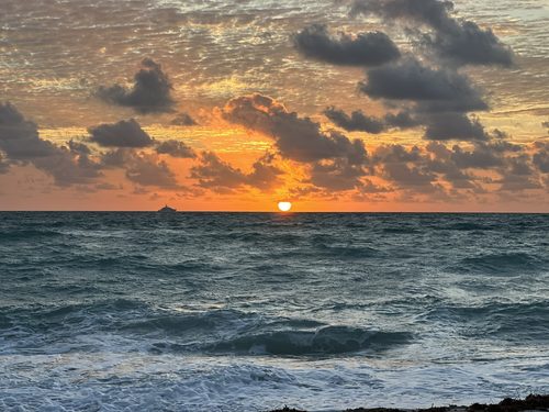 Sunset over the water with a yacht on the horizon